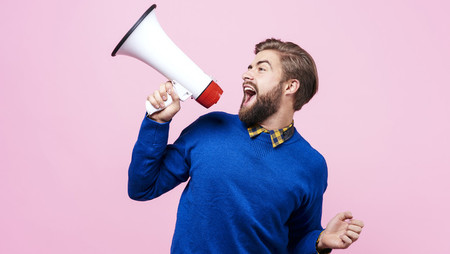 Cheerful young man shouting into a megaphone against a pink background