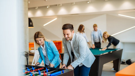 A group of coworkers playing foosball and billiards in office break room