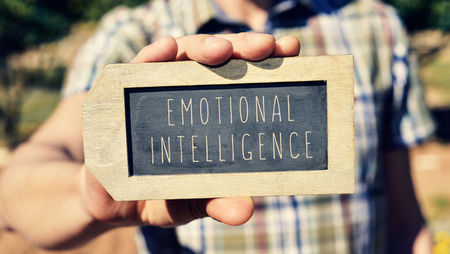 Close-up of a man holding a lapel-shaped chalkboard that has 'emotional intelligence' written on it