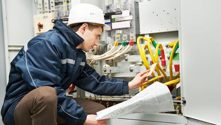 An electrician checking cabling and blueprints