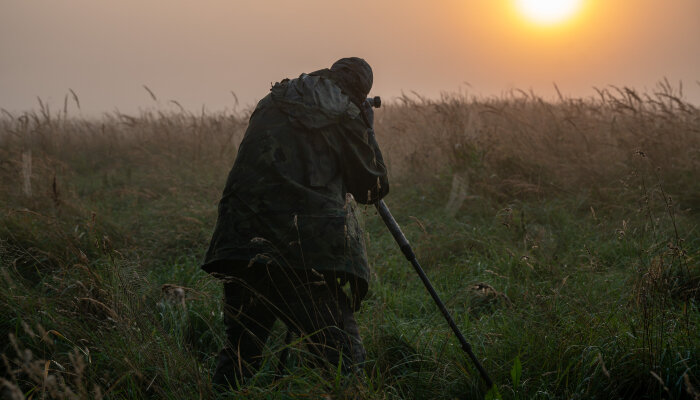 A wildlife biologist with a camera in an expansive field