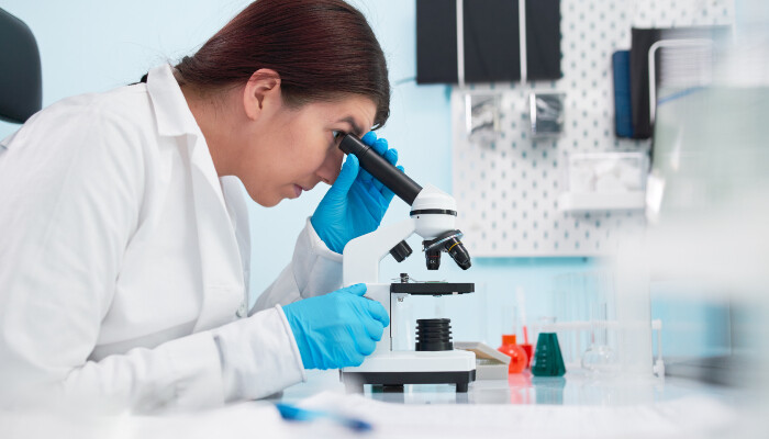 A female epidemiologist looking through a microscope in a laboratory